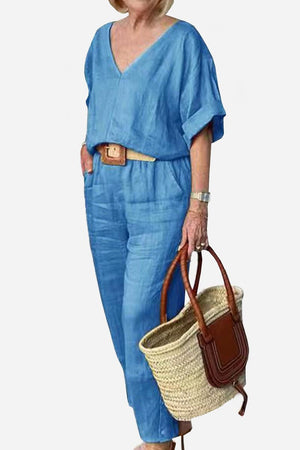 Woman wearing blue V-neck cotton two-piece trouser set with rolled sleeves and carrying a woven straw handbag.