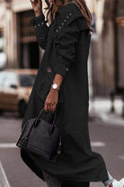 Woman wearing a black sleek minimalist hooded coat with oversized fit carrying a black handbag on city street