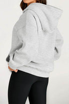 woman wearing gray oversized fleece-lined hoodie with hood and black leggings back view