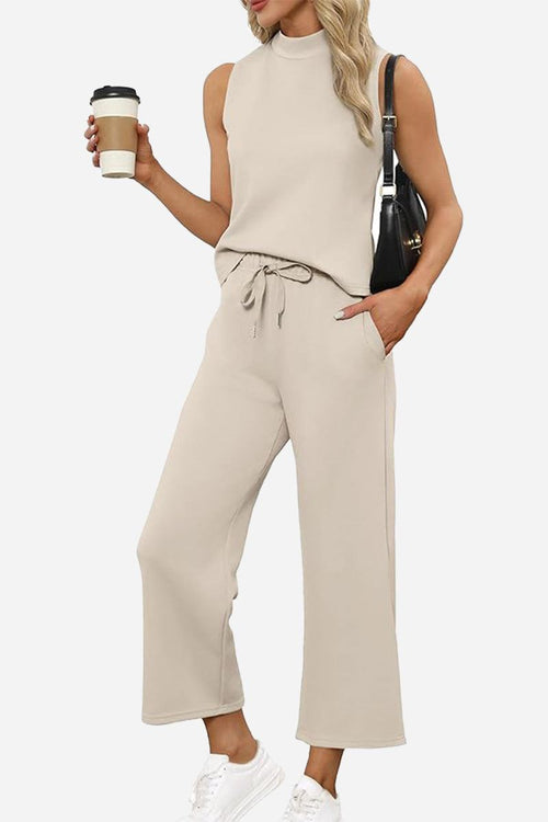Woman wearing beige Cotton Chic Sleeveless two-piece outfit with sleeveless top and wide-leg pants holding coffee cup and black handbag