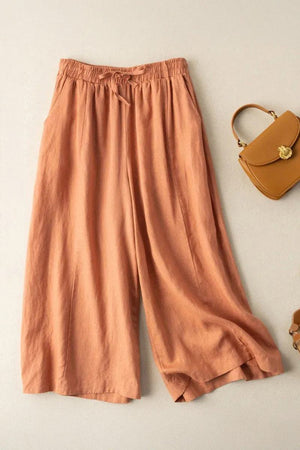 Wide-leg cotton linen Tuscany pants in warm terracotta shade with elastic waistband and tie detail, styled with a tan handbag on light background