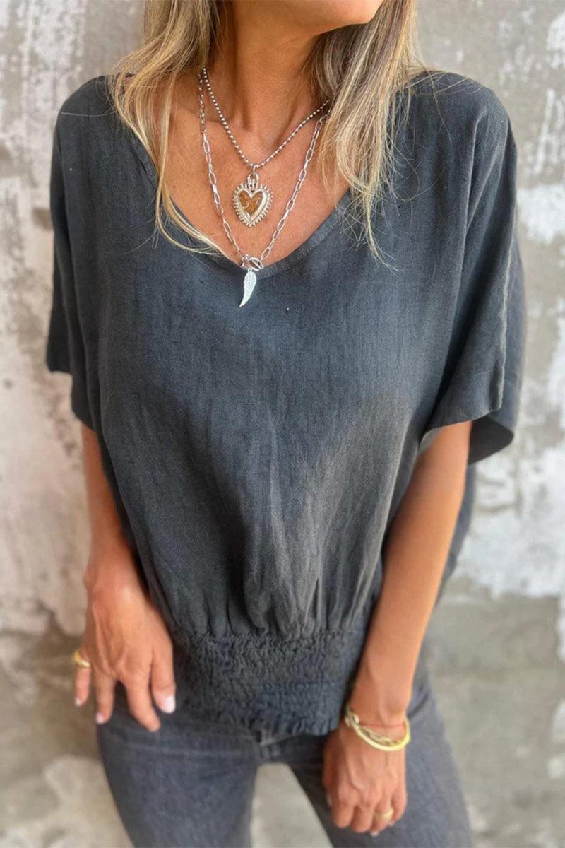 Women wearing a charcoal grey pure linen short-sleeve blouse with V-neck and smocked waist detail.
