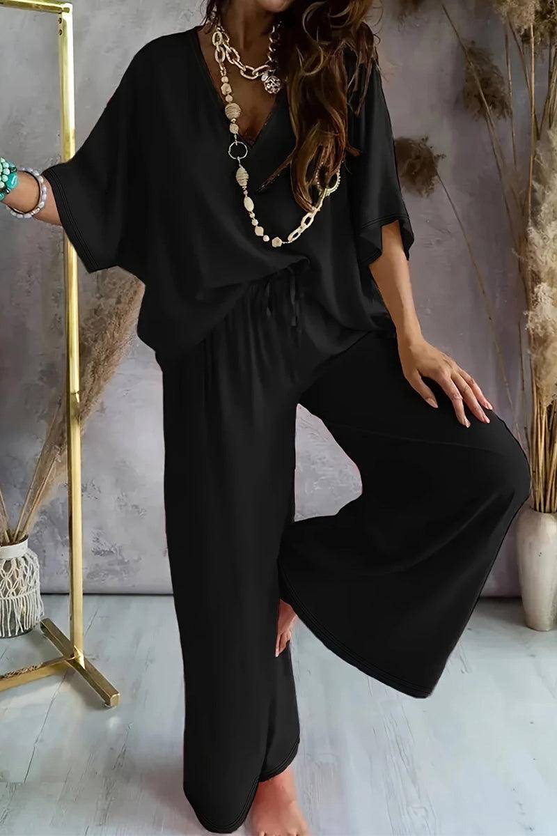 Black two-piece pantsuit with V-neck top and wide-leg pants styled with layered necklaces