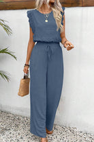 Woman wearing a blue elegant two-piece set with lace details, featuring a sleeveless ruffled top and wide-leg pants.