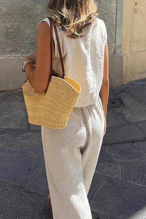 woman wearing beige cotton-linen blend two-piece summer outfit with woven straw bag walking outdoors