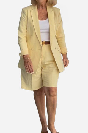 Woman wearing stylish blazer and shorts two-piece set in light yellow with white top and belt.