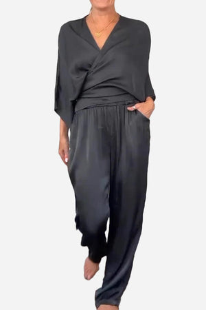 Woman wearing black Satin Wrap Lounge two-piece set with V-neck top and relaxed pants.
