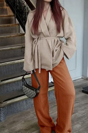Woman wearing mix-match lounge-to-travel set with beige belted top and rusty orange wide-leg pants carrying handbag
