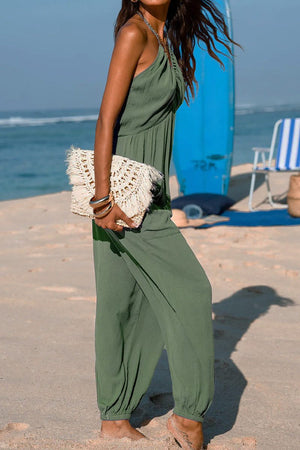 Woman wearing green Sunshine On Sand halter-neck wide-leg jumpsuit on the beach holding a woven clutch bag