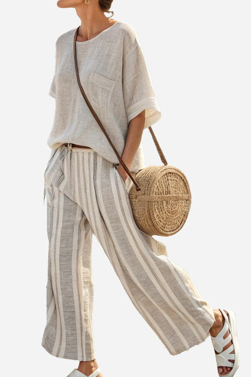 Woman wearing Coastal Comfort Linen two-piece set with striped wide-leg pants and loose short-sleeve top carrying round woven bag.