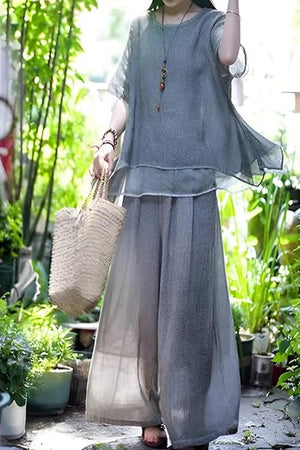 Woman wearing flowing Provence cotton linen blend layered top and wide-leg trousers set outdoors carrying woven bag