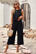 Woman wearing black Villa Lounge Linen Set sleeveless cropped top and wide-leg pants with sunglasses and straw handbag outdoors