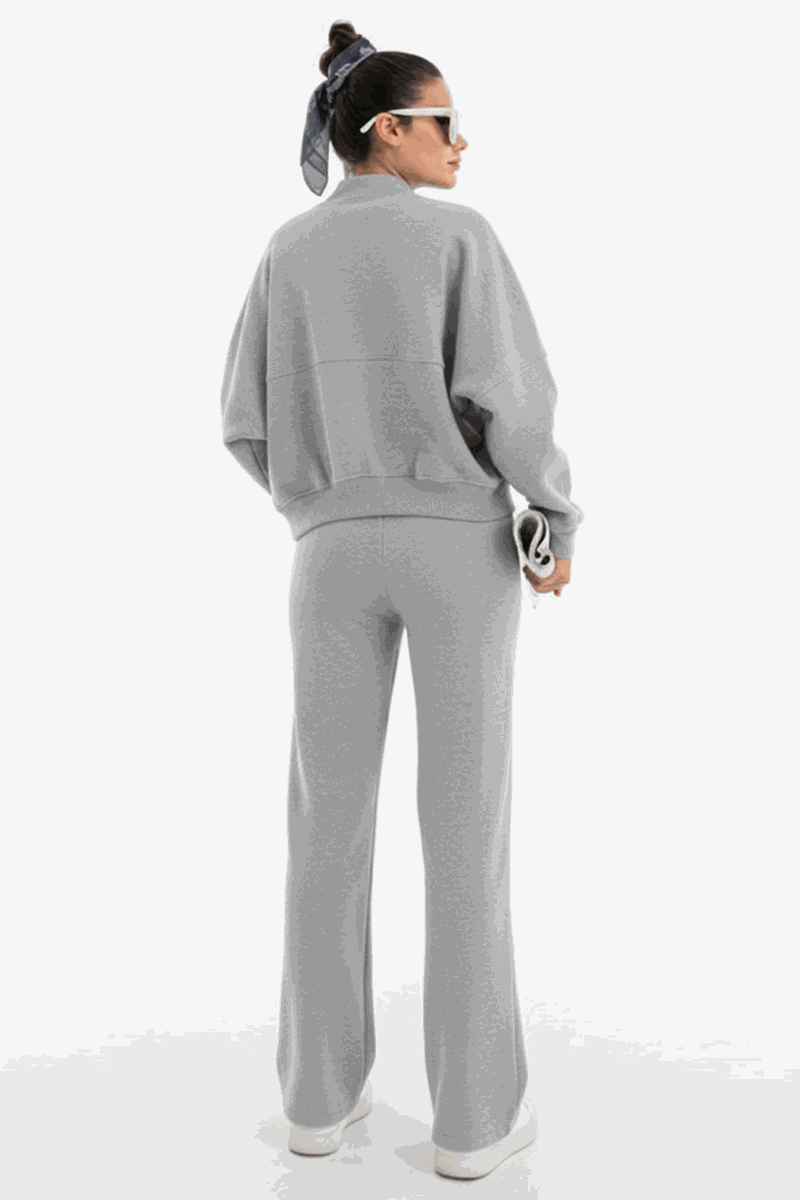 Woman wearing The Voyager Zip Set in light gray, featuring a relaxed zip-front sweatshirt and wide-leg joggers with pockets, styled for comfort and travel.