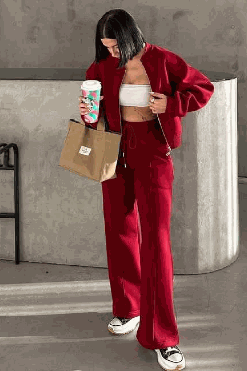 Woman wearing The Voyager Zip Set red zip-front sweatshirt and wide-leg joggers, carrying tote and holding coffee cup
