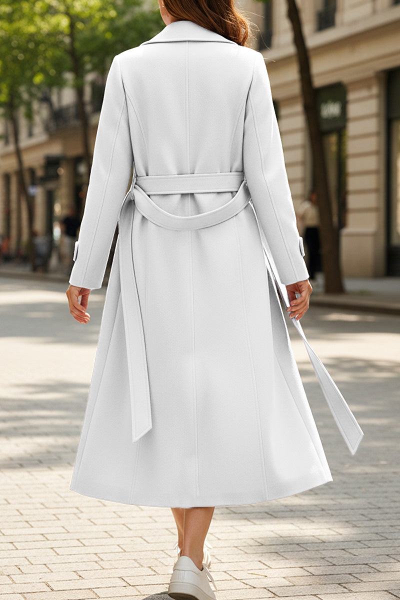 Woman wearing a timeless retro belted trench coat in white, showing back view with full-length cut and waist belt on city street.