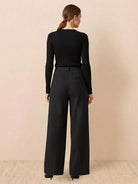 Woman wearing black thermal wool blend trousers with wide-leg fit and elastic back waist standing against a neutral background