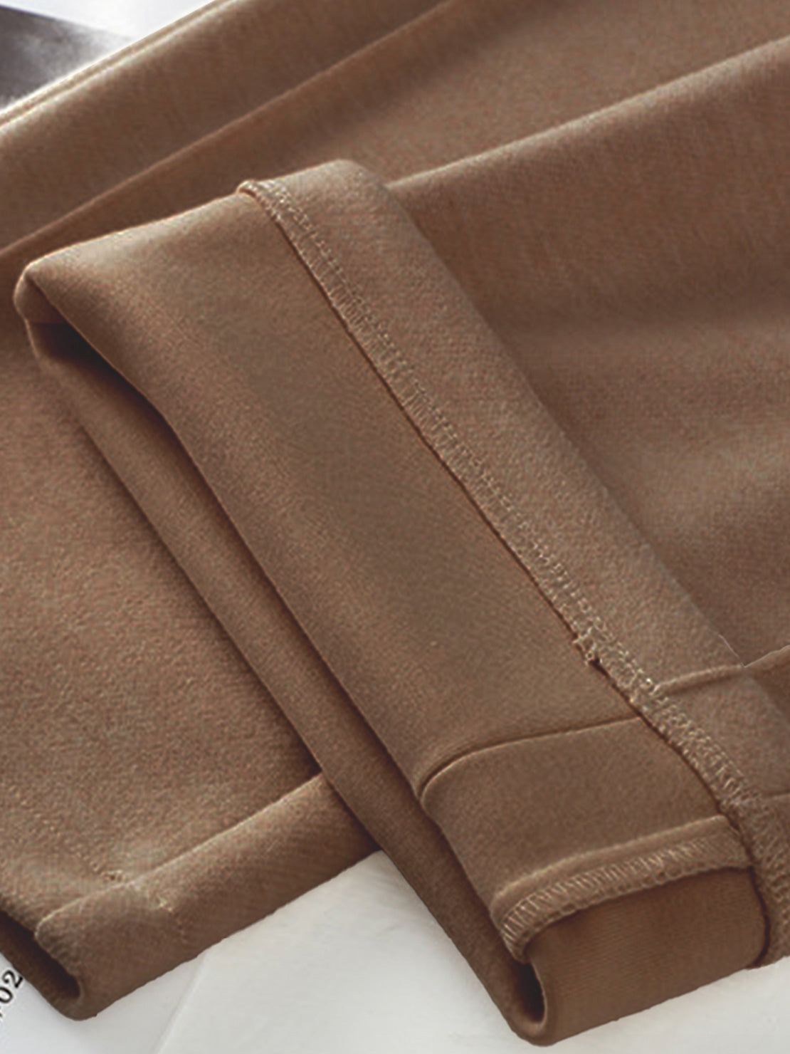 Close-up of brown thermal wool blend trousers fabric with folded cuffs and stitching detail