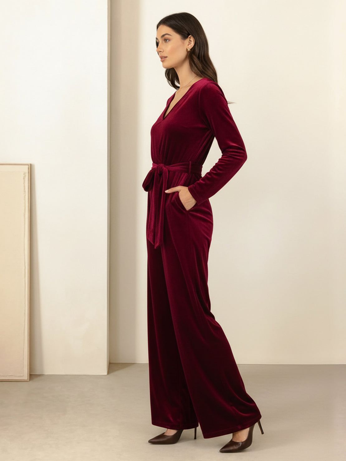 Woman wearing deep V-neck velvet suit with long sleeves, removable waist tie, and wide-leg pants with side pockets in structured yet flexible fabric