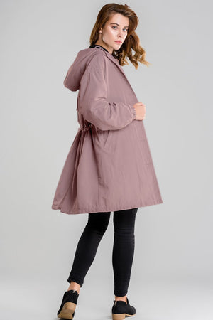 Woman wearing oversized mauve water-resistant windbreaker jacket with hood and black leggings against gray background