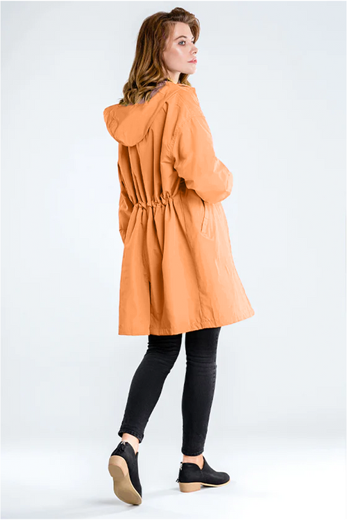 Woman wearing an orange water-resistant oversized hooded windbreaker rain jacket with black leggings and shoes, viewed from the back.
