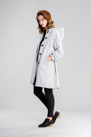 Woman wearing a light gray water-resistant oversized hooded windbreaker rain jacket with black buttons and black leggings.