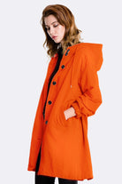 Orange water resistant oversized windbreaker with hood and button closure on female model