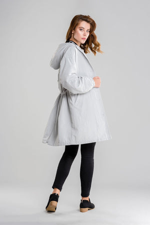 woman wearing light gray oversized water-resistant windbreaker jacket with hood and black pants against gray background