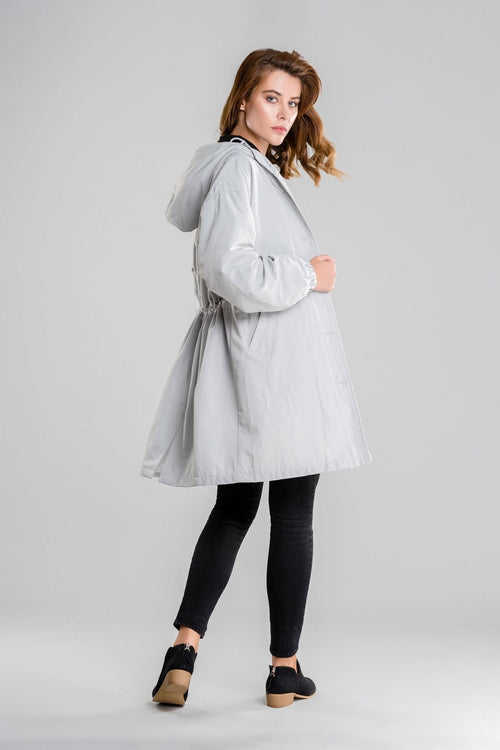 woman wearing light gray oversized water-resistant windbreaker jacket with hood and black pants against gray background