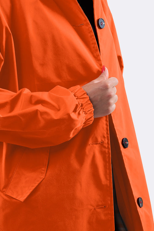 Close-up of a person wearing an orange water-resistant oversized windbreaker with button closure and elastic cuffs