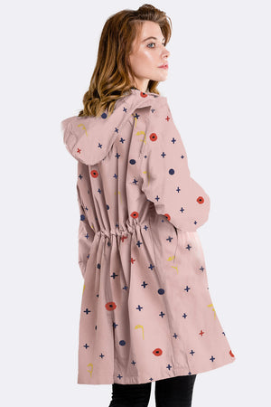 Woman wearing water-resistant oversized windbreaker with hood and colorful pattern on light pink fabric