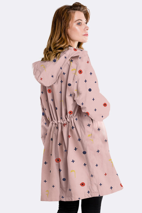 Woman wearing water-resistant oversized windbreaker with hood and colorful pattern on light pink fabric