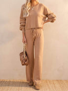 Woman wearing a beige round neck loose fit cozy two-piece set with long sleeves and wide-leg pants, holding a brown handbag