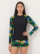Woman wearing a swim shorts rash guard set with long raglan sleeves and matching printed boyshort bottoms at the beach