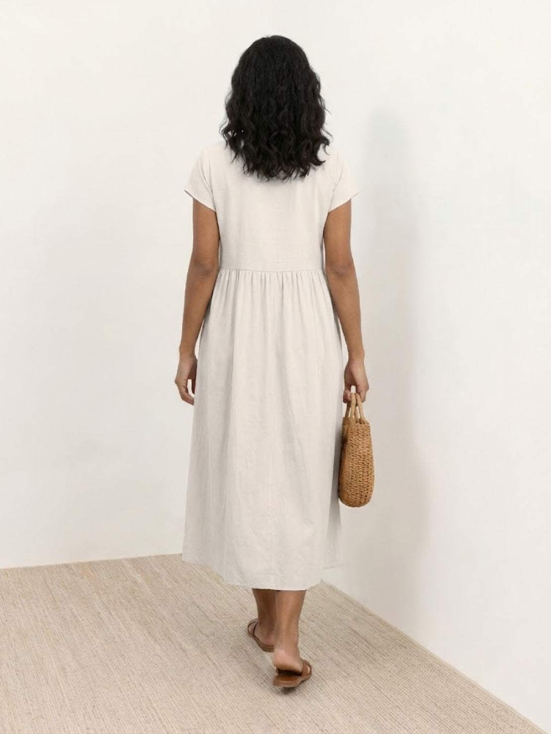 Woman wearing capped-sleeve voluminous pleated midi dress with flowing skirt and pocket detail