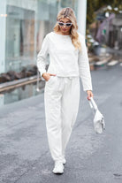 Woman wearing cotton-linen monochrome relaxed longline top and wide-leg pants set walking outdoors with sunglasses and white handbag