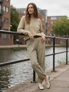 Woman wearing European Minimalism relaxed sweater top and trouser set in neutral khaki by a canal walkway