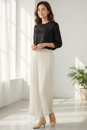 Woman wearing Garden Soirée cotton-silk pleated wide-leg trousers with black top indoors