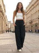 Woman wearing black high-waist palazzo pants with pockets and white crop top walking outdoors in city street