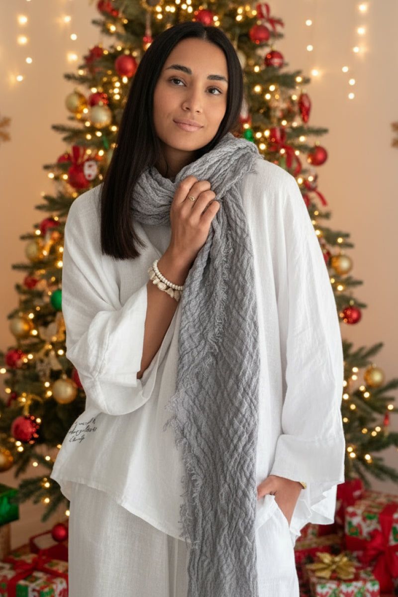 Woman wearing lightweight gray linen scarf in front of decorated Christmas tree