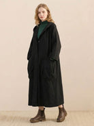 Woman wearing oversized black water-resistant windbreaker jacket with hood and large pockets, styled with boots.