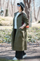 Woman wearing oversized olive green water resistant windbreaker jacket with hood and large pockets outdoors