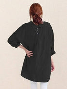 White oversized linen shirt with relaxed fit and back button detailing hanging on a wooden hanger against a white background