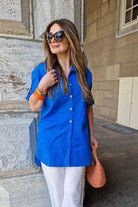 Woman wearing oversized linen shirt in bright blue with white pants and sunglasses outdoors