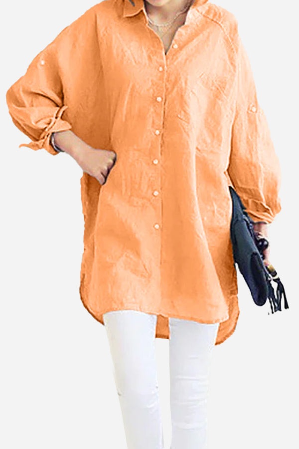 Woman wearing oversized orange linen shirt with long sleeves and white pants, holding black clutch bag