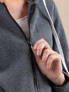 Close-up of a person zipping a gray oversized long zip sweatshirt hoodie with white drawstrings and fleece lining.