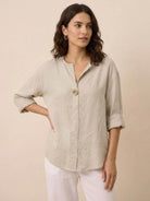 Woman wearing a beige pure linen age-defying shirt with button detail and rolled sleeves.