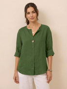 Woman wearing green pure linen age-defying shirt with button detail and rolled sleeves, styled with white pants.