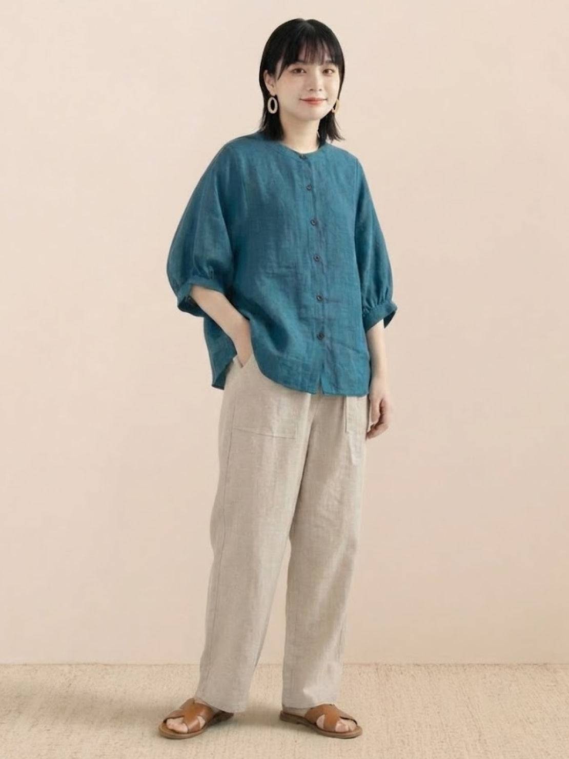 Relaxed loose breathable linen blouse in teal with button-down front and 3/4 sleeves worn with beige pants
