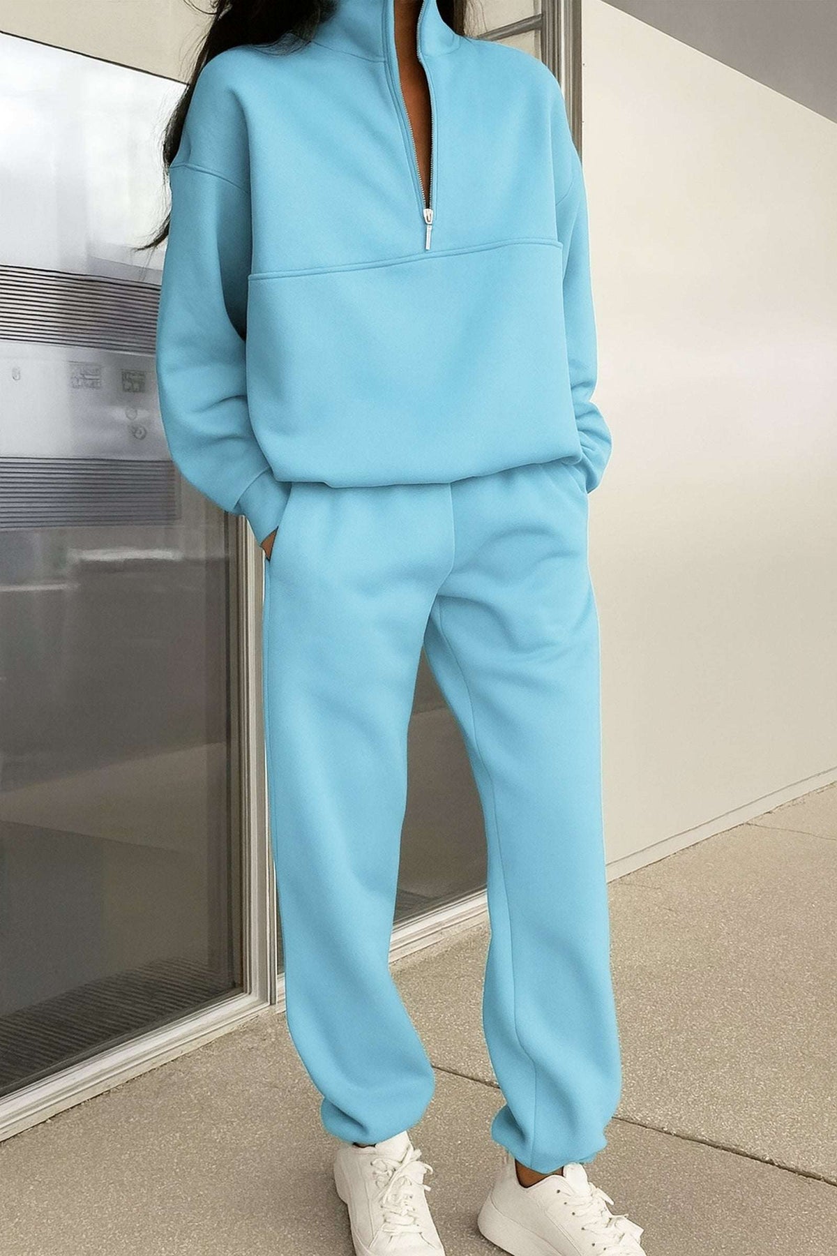 Woman wearing light blue cotton blend tracksuit with zip neckline and white sneakers standing indoors