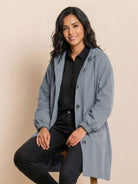 Woman wearing oversized grey Rain Couture Windbreaker over black outfit sitting on stool